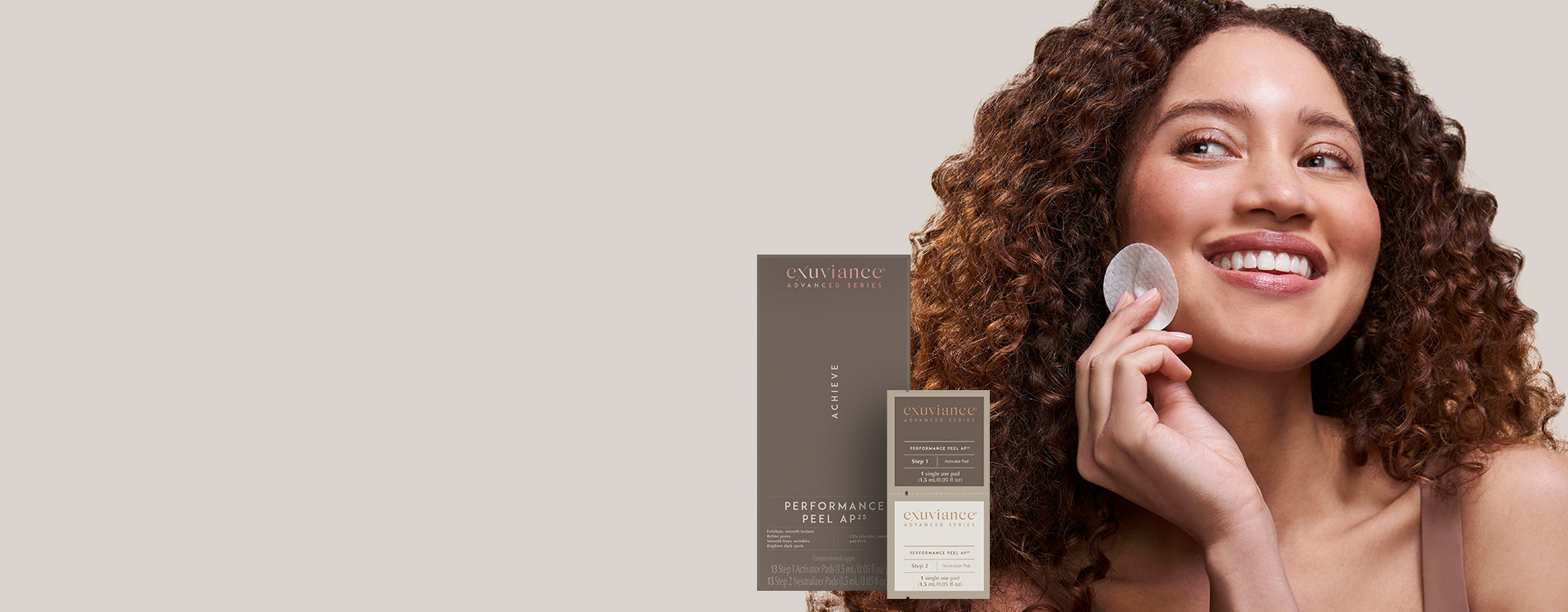 A woman with brown curly hair wearing a tank top and smiling holding a Performance Peel AP 25 peel pad to her face, against a light beige background.