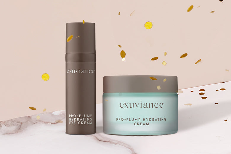 Exuviane Pro-Plump Hydrating Cream and Eye Cream on a marble counter top against a light beige background with gold glitter flying in the air.